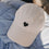 Beige Cap mit schwarzem Herz-Stick liegend auf blauer Jacke