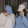 Zwei Frauen mit Caps: blaue „easy peasy“ Cap und beige Cap mit Herz-Stick