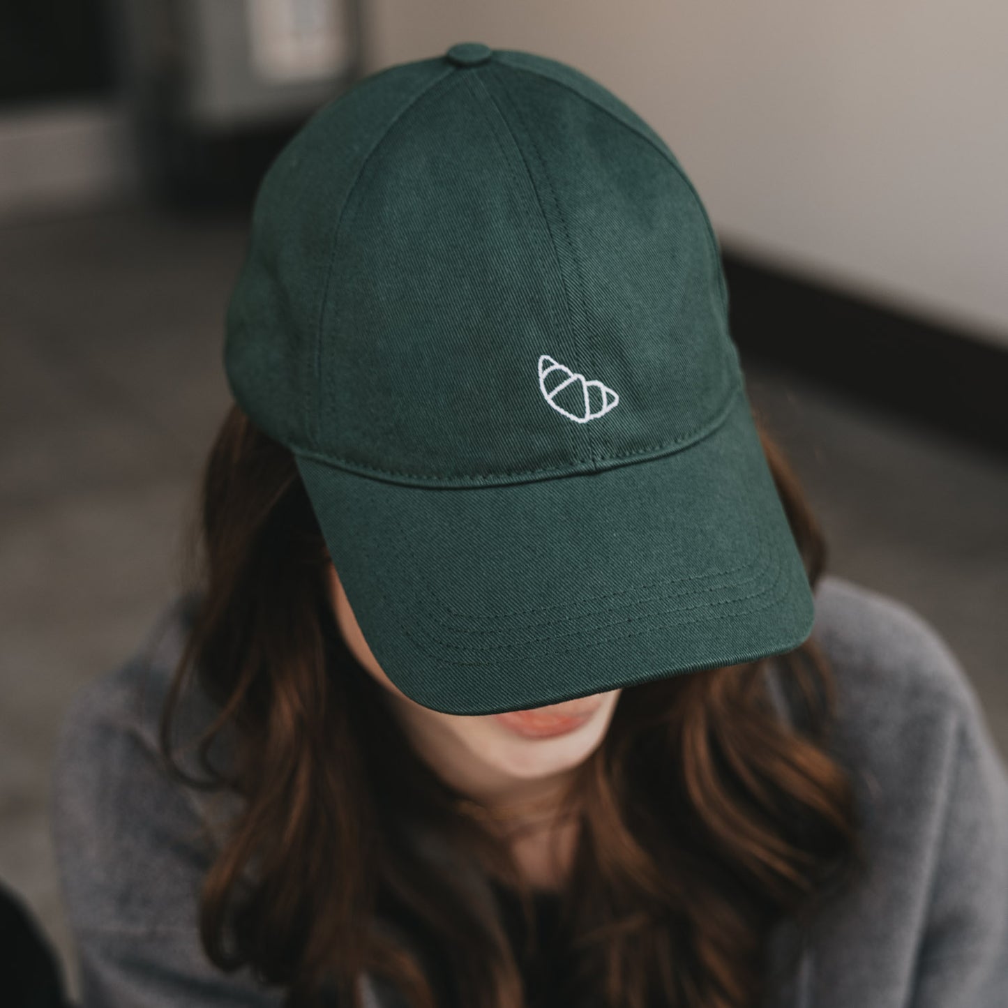 Dunkelgrüne Cap mit weißer Croissant-Stickerei, getragen von Frau