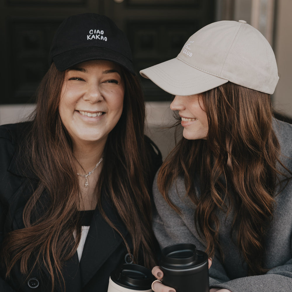 Zwei Frauen mit Caps und Coffee-to-go, eine trägt schwarze „Ciao Kakao“ Cap