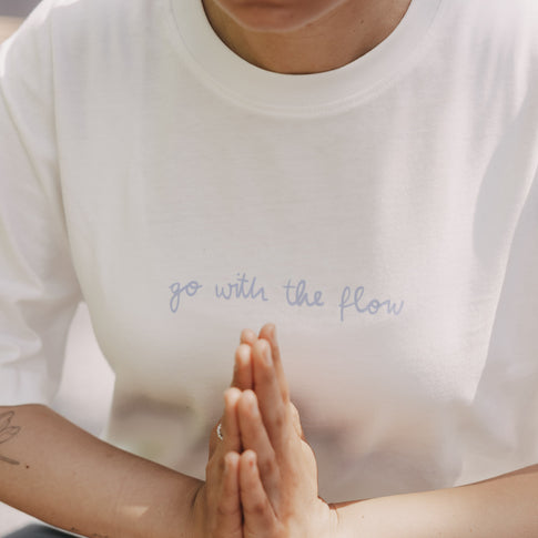 Detailansicht: weißes T-Shirt mit Schriftzug „go with the flow“ vorne, Hände in Gebetshaltung