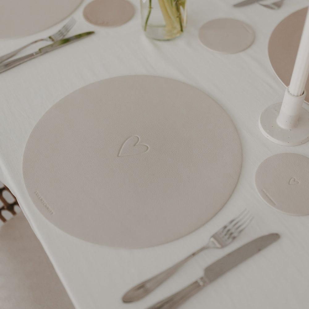 Cremefarbenes Platzset mit Herzprägung und passendem Untersetzer auf hell gedecktem Tisch