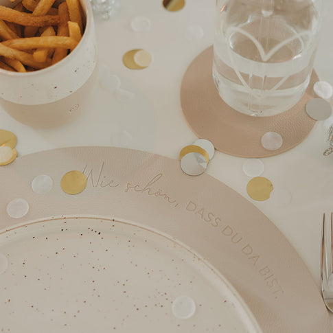 Festlich gedeckter Tisch mit cremefarbenem Platzset „Wie schön, dass du da bist“, Konfetti, Teller, Glas und Pommes