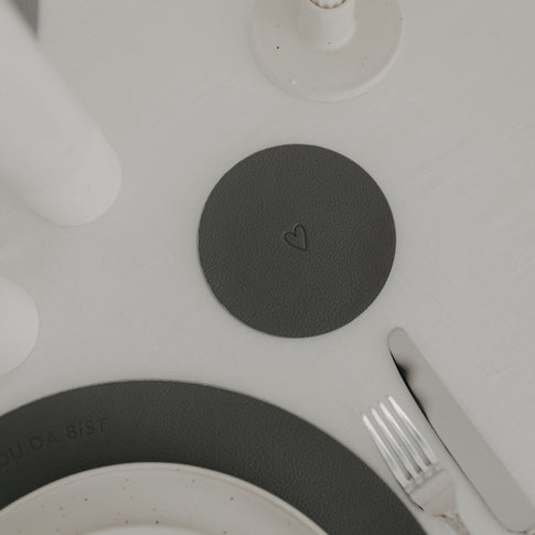 Wendbarer Untersetzer in Dunkelgrau mit eingeprägtem Herzmotiv auf gedecktem Tisch.