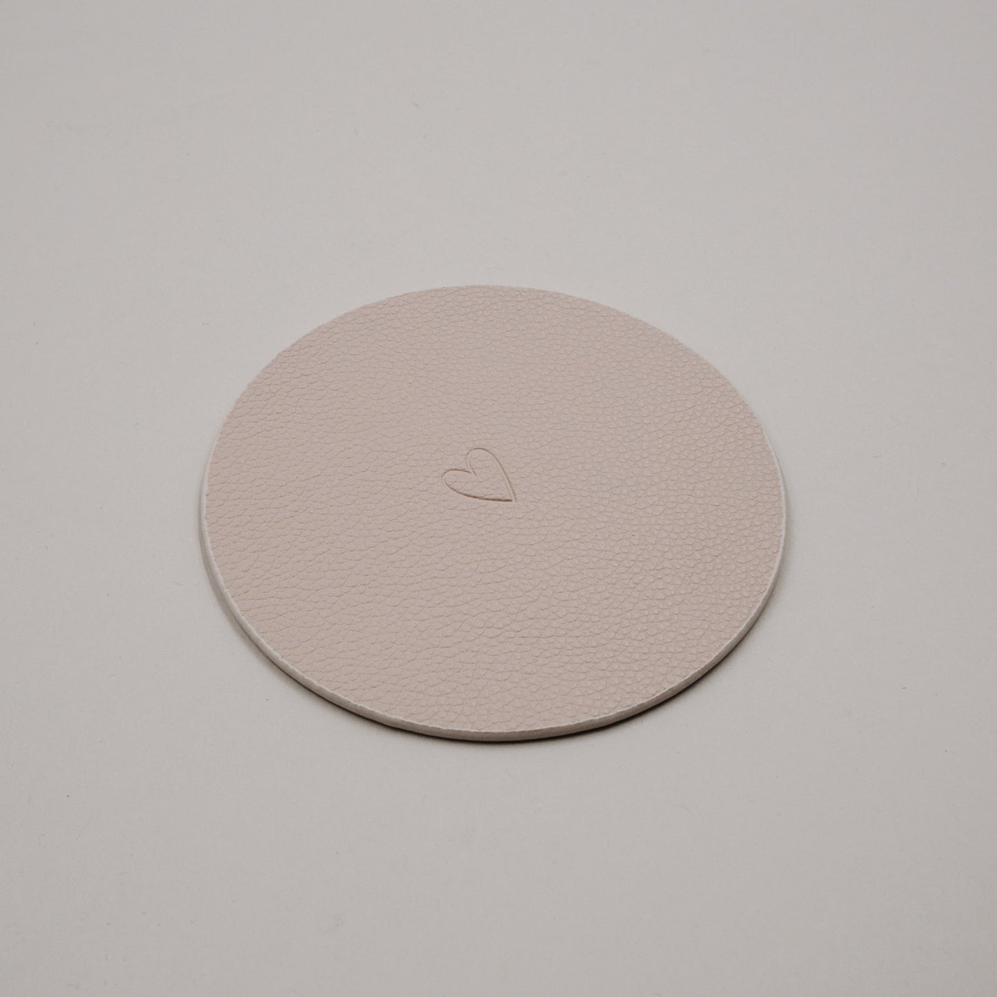 Wendbarer Untersetzer in Creme mit Herzprägung, runde Form und feine Lederstruktur.