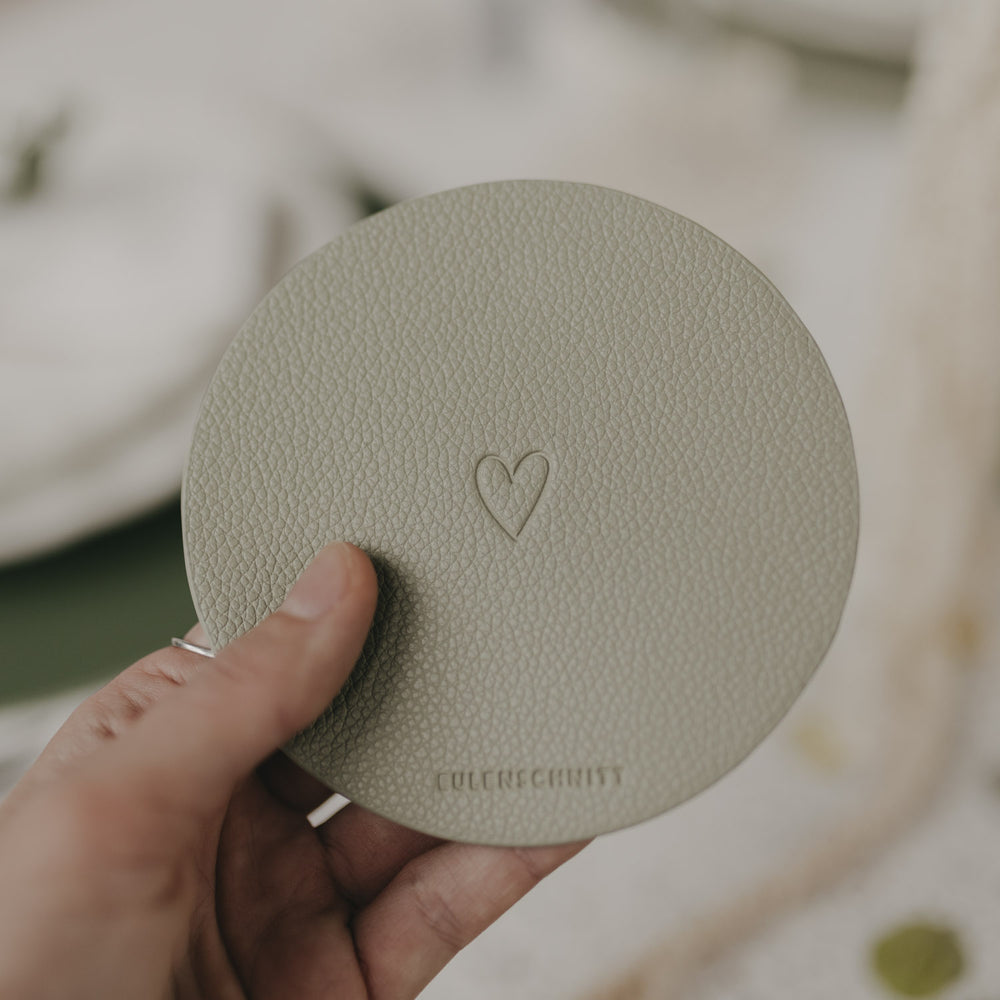 Hand hält hellgrünen Untersetzer mit Herzprägung und Eulenschnitt-Logo.