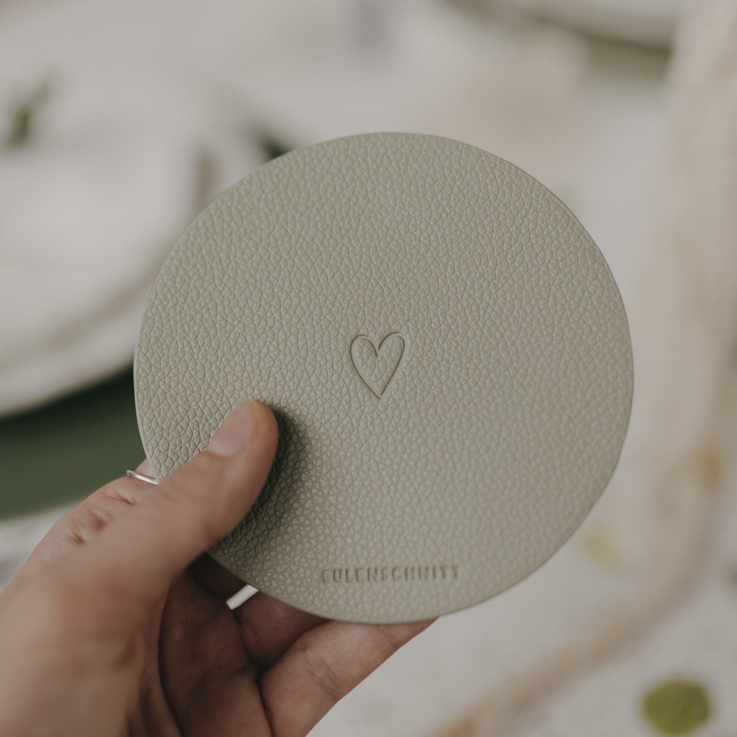 Hand hält hellgrünen Untersetzer mit Herzprägung und Eulenschnitt-Logo.