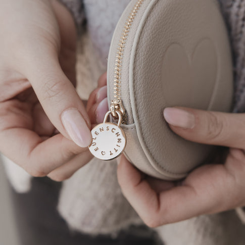 Detailaufnahme Reißverschlussanhänger mit Eulenschnitt Logo am cremefarbenen Portemonnaie
