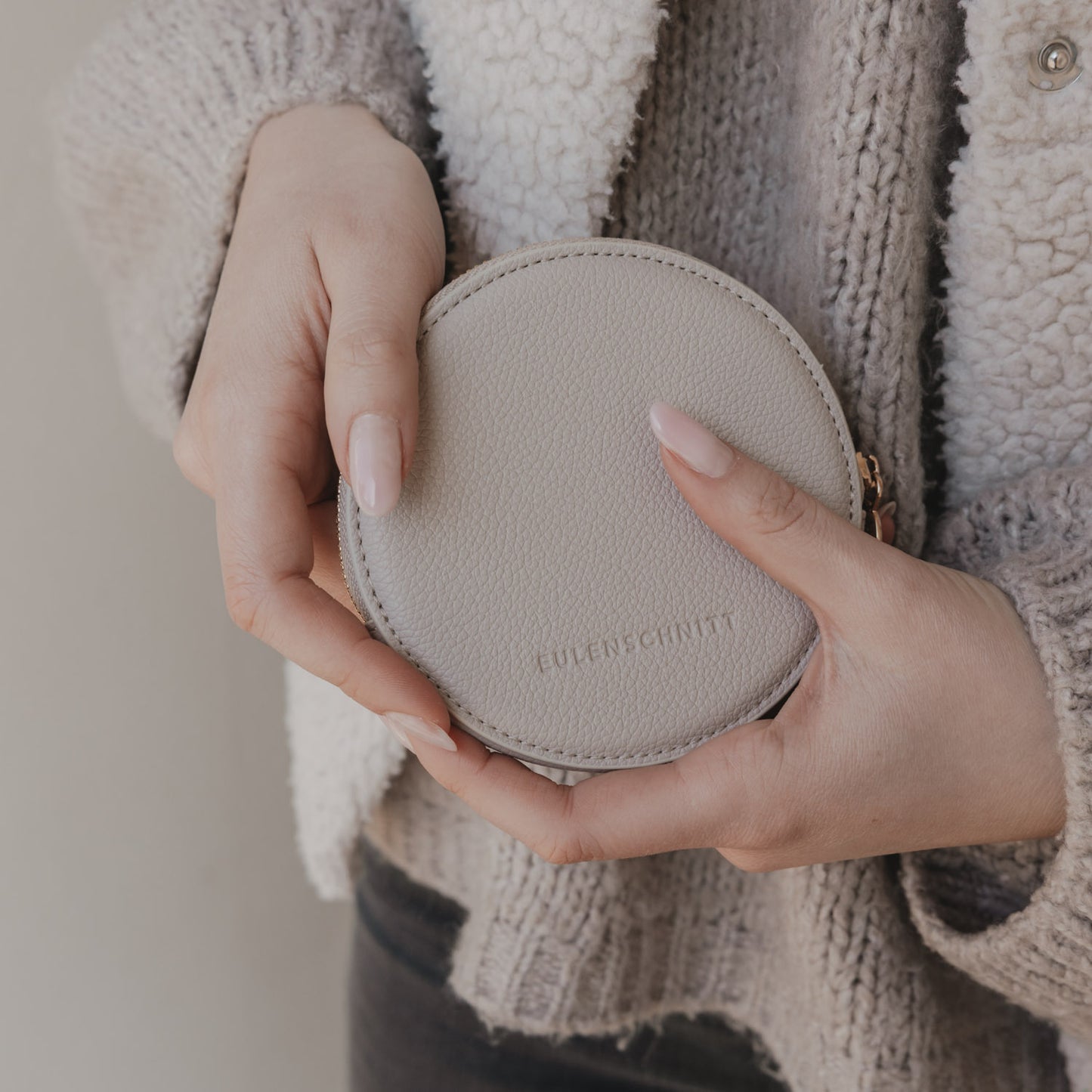 Rückseite rundes Portemonnaie in Creme mit Eulenschnitt Prägung in der Hand gehalten