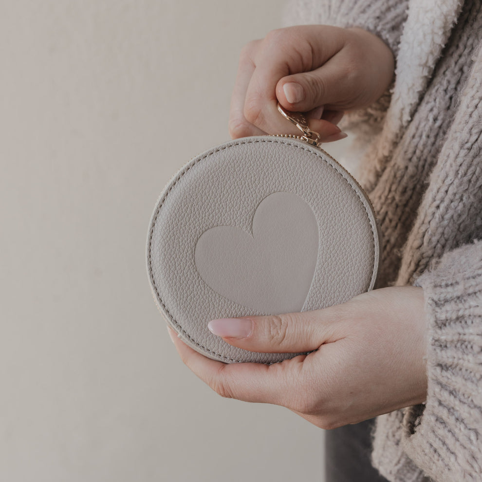 Rundes Herz-Portemonnaie in Creme in Händen gehalten mit goldenem Reißverschluss