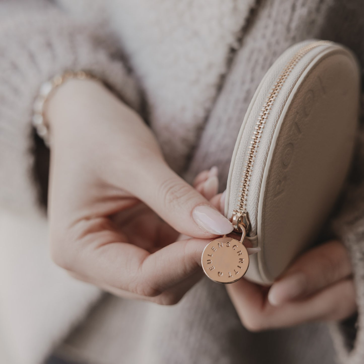 Beiges rundes Portemonnaie mit BOTOX MONEY Prägung, in Händen gehalten, goldener Zipperanhänger.