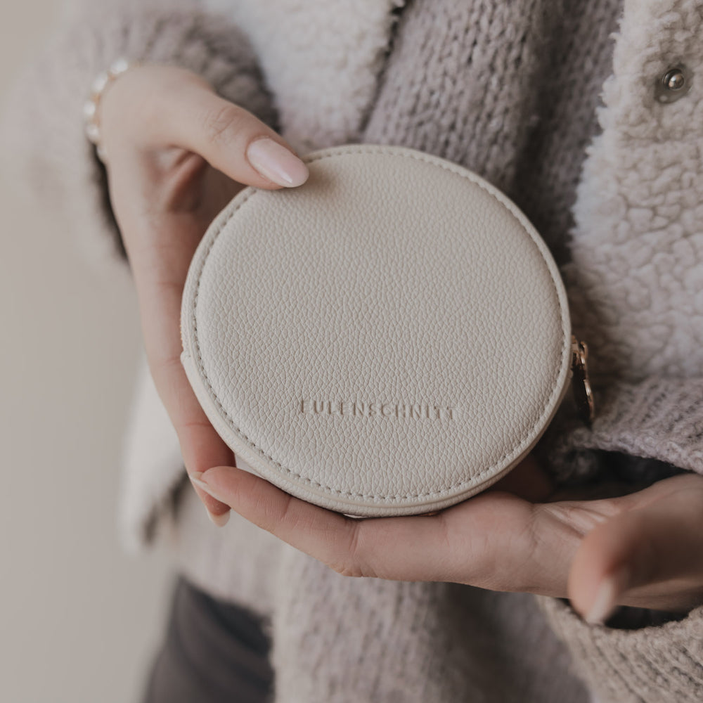 Rückseite des beigen runden Portemonnaies mit geprägtem Eulenschnitt-Logo, in Händen gehalten.