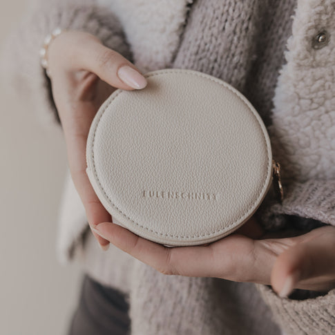 Rückseite des beigen runden Portemonnaies mit geprägtem Eulenschnitt-Logo, in Händen gehalten.