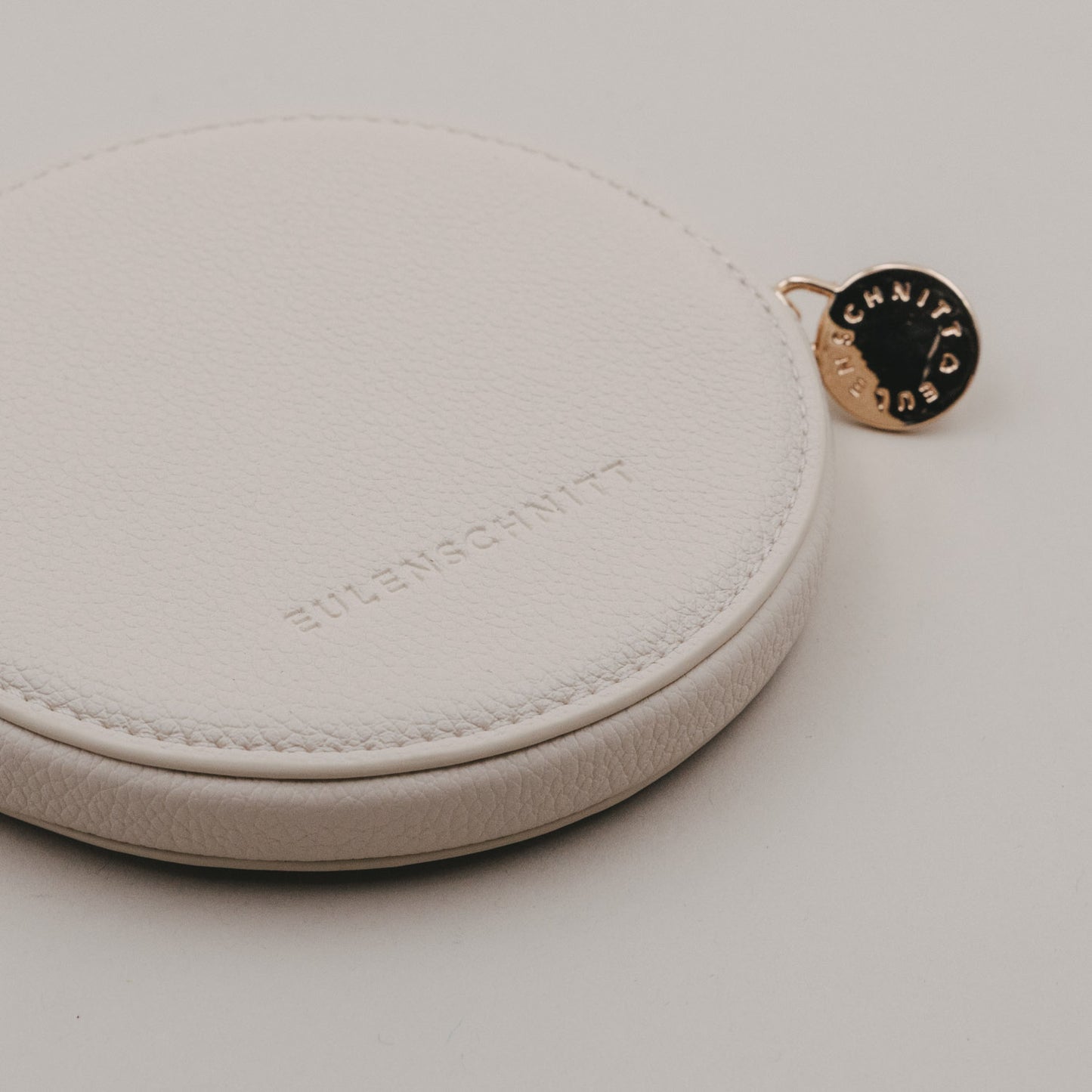 Rückseite des beigen runden Portemonnaies mit geprägtem Eulenschnitt-Logo, in Händen gehalten.