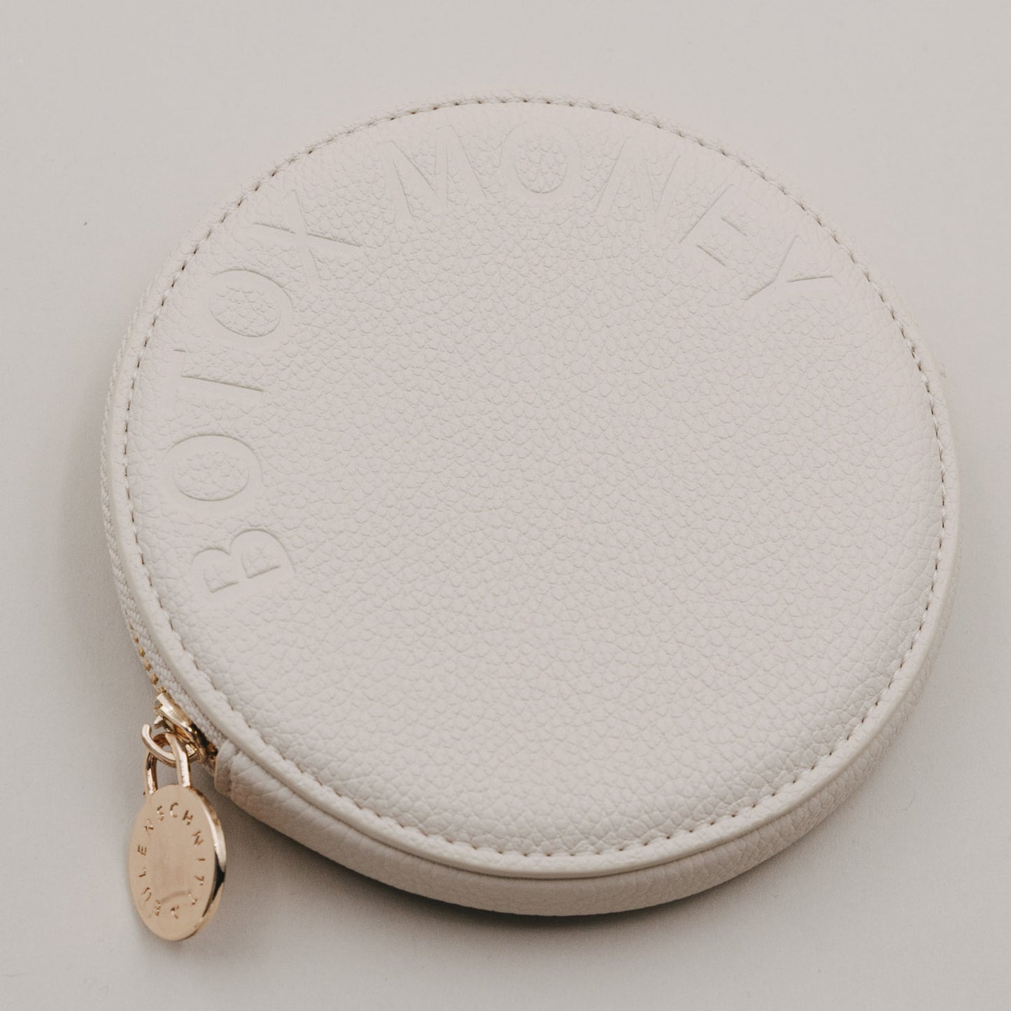 Rundes Portemonnaie in Beige mit geprägtem Schriftzug BOTOX MONEY und goldenem Reißverschlussanhänger.