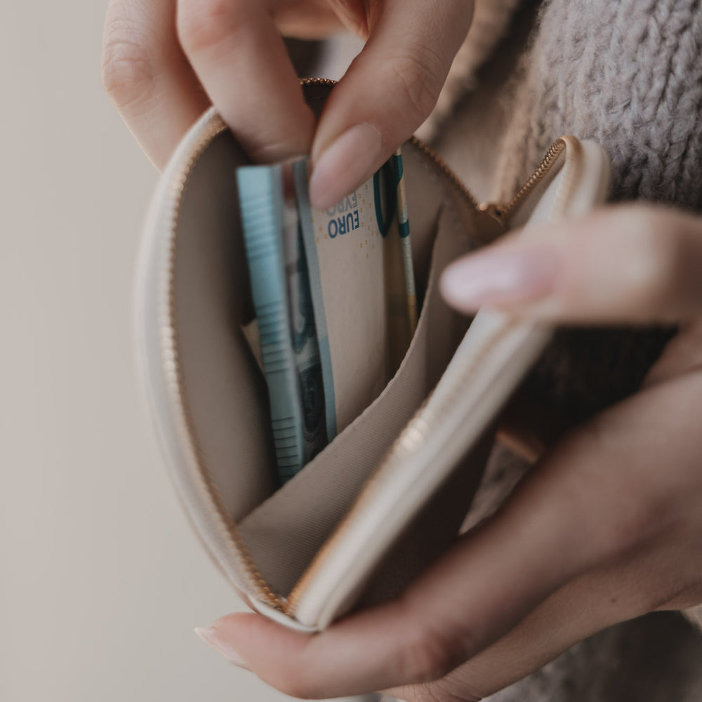 Rundes Portemonnaie mit BOTOX MONEY Prägung, in Händen gehalten, beige Struktur und goldener Reißverschluss.