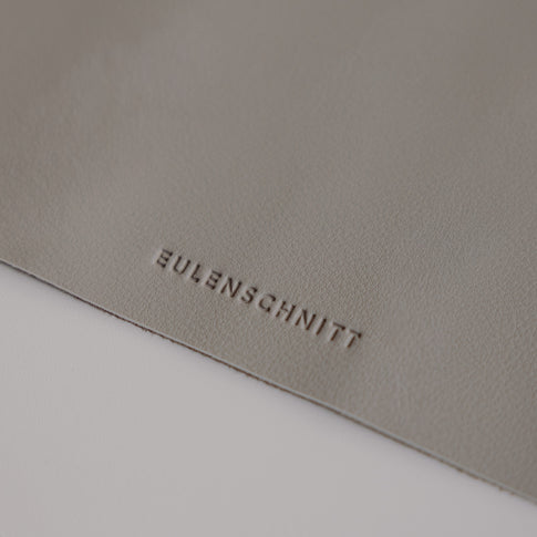 Detailaufnahme Logo Eulenschnitt auf grauer Schreibtischunterlage, hochwertige Lederoptik