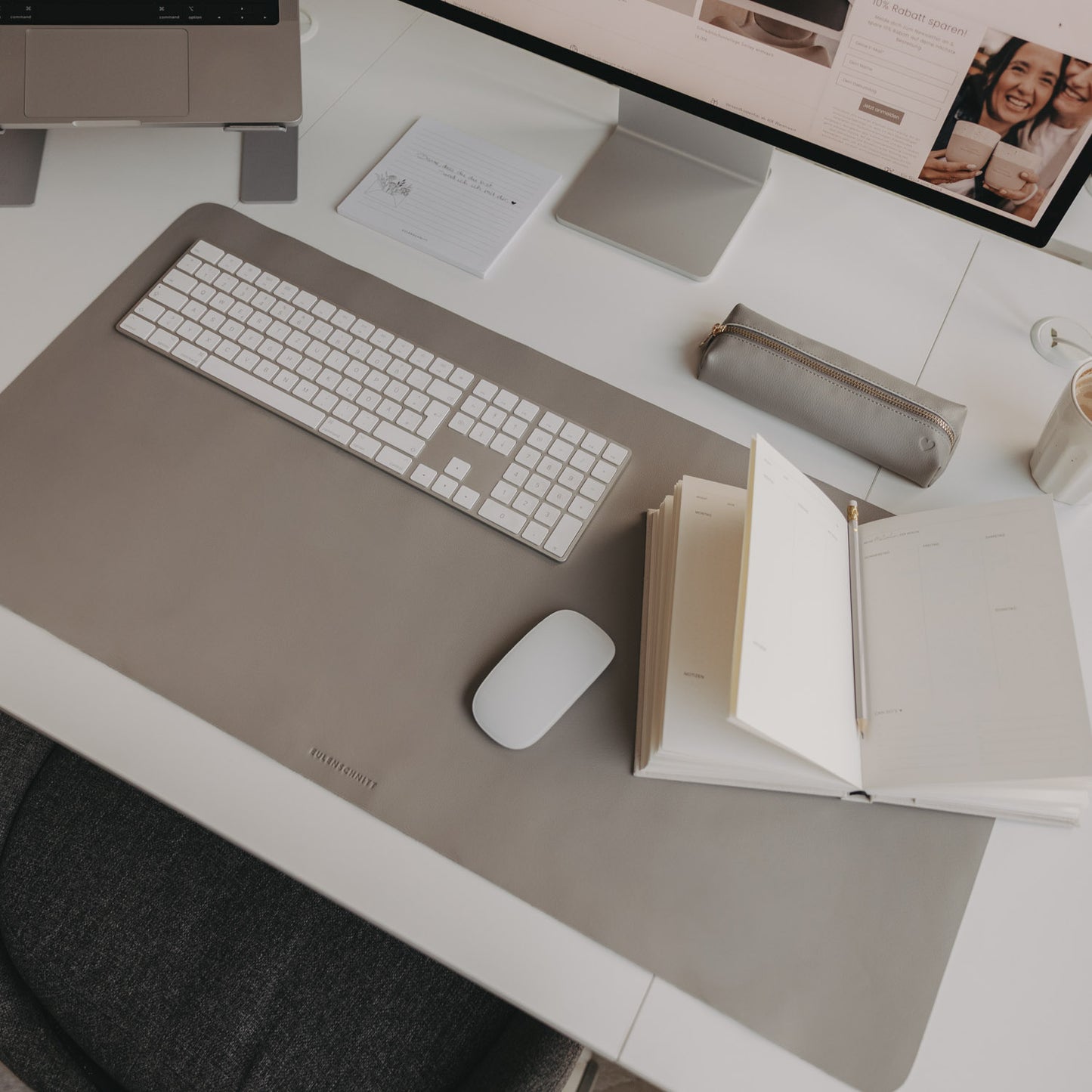 Arbeitsplatz mit grauer Schreibtischunterlage Herz, Laptop, Monitor und Notizbuch minimalistisch