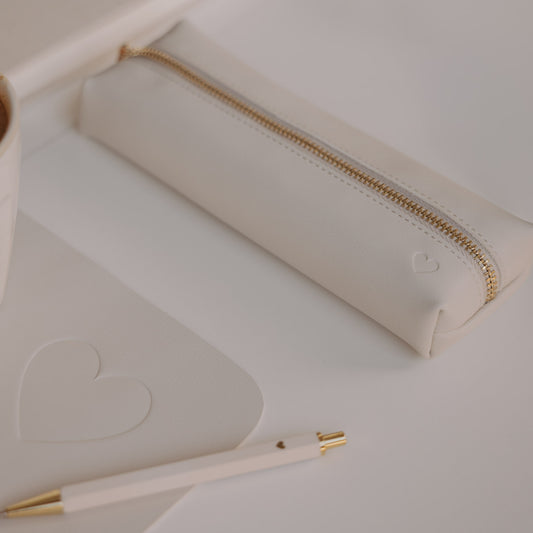 Federtasche creme mit Herzprägung und goldenem Reißverschluss von Eulenschnitt neben Notizbuch und Stift