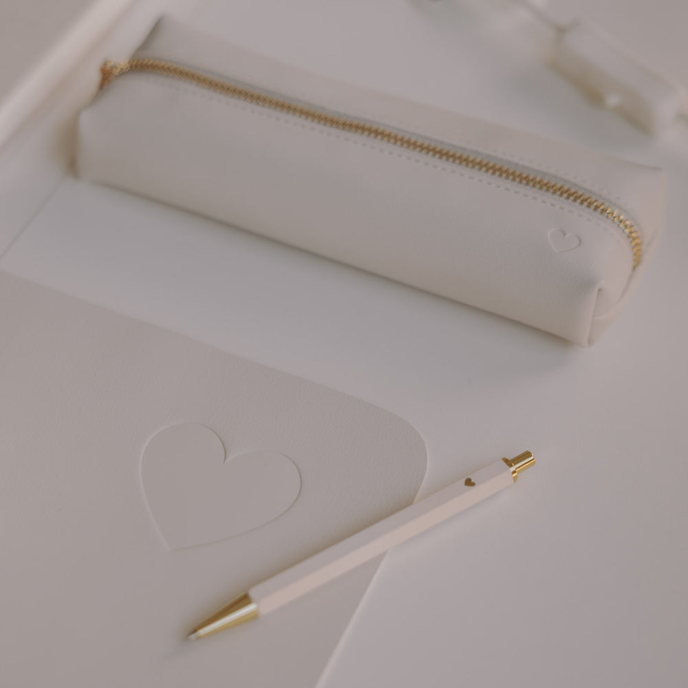 Federtasche creme mit Herzprägung auf Schreibtisch neben Notizbuch und Stift