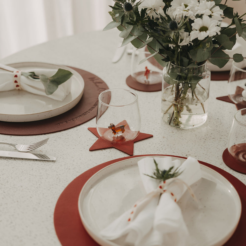 Festlich gedeckter Tisch mit roten Platzsets, Stern-Untersetzer, Gläsern und Blumen