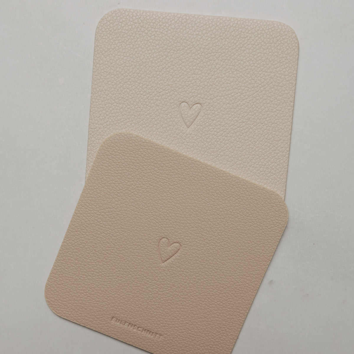 Zwei quadratische Untersetzer in Creme und Beige mit abgerundeten Ecken und geprägtem Herz