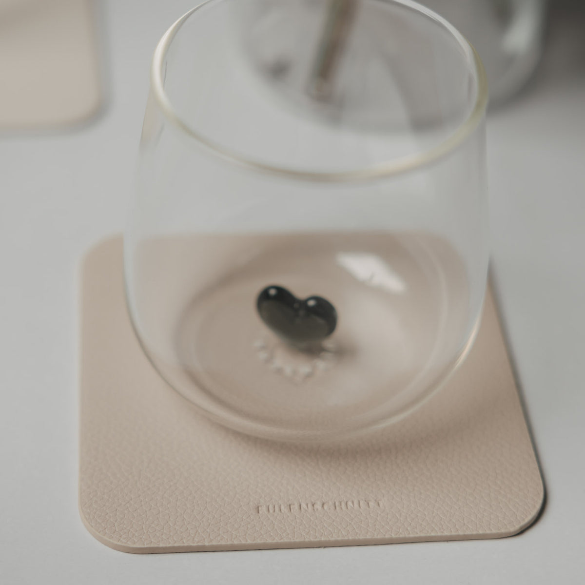 Glas mit schwarzem Herzdetail auf einem beigen quadratischen Untersetzer