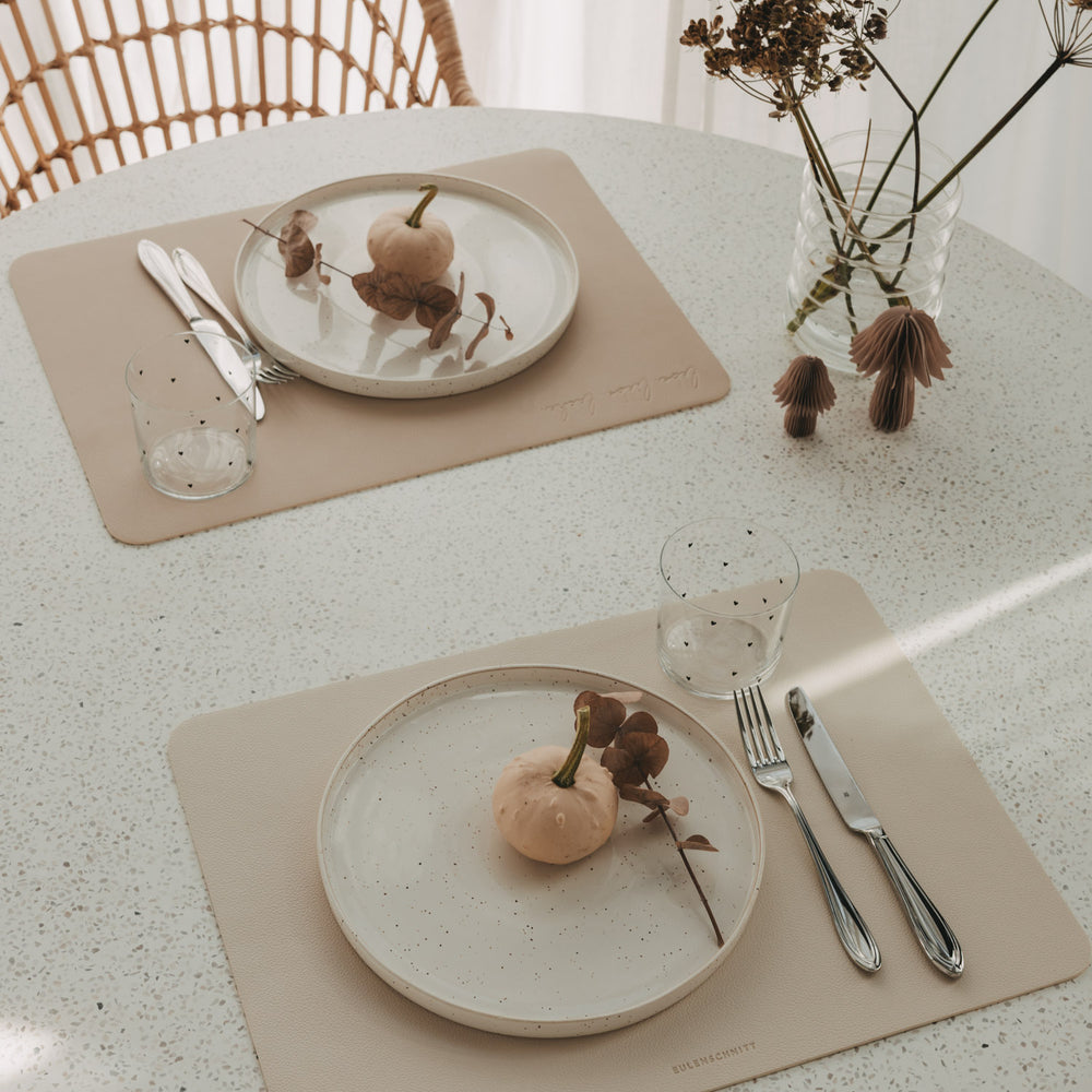 Zwei wendbare Platzsets in Creme und Beige mit Tellern, Besteck und Gläsern auf Esstisch