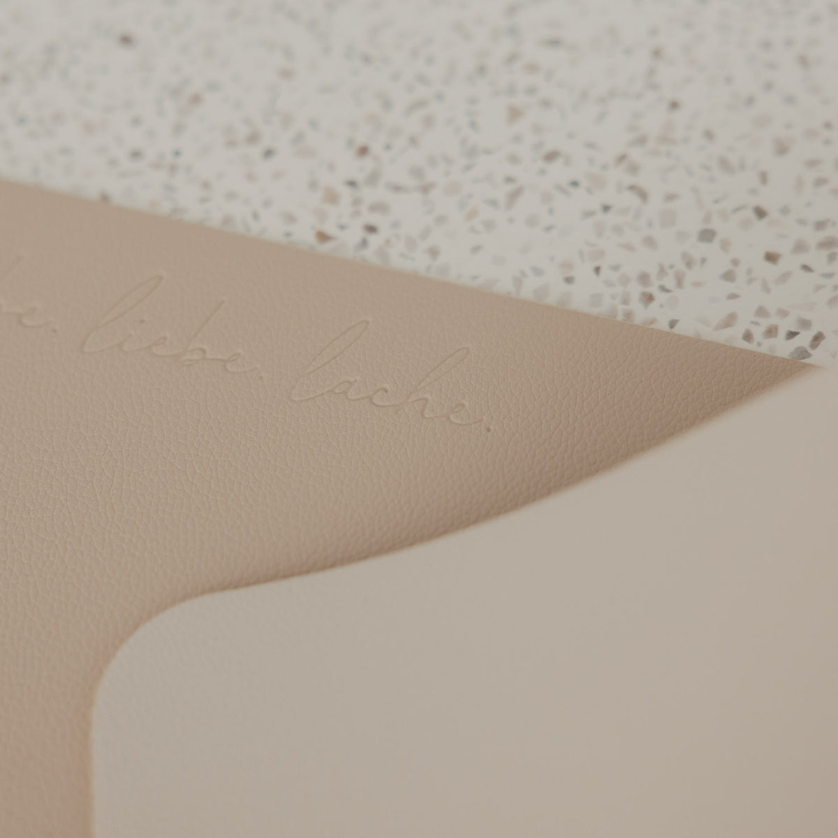 Detailaufnahme des beigen Platzsets in Lederoptik mit geprägtem Schriftzug „lebe liebe lache“
