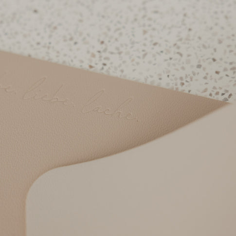 Detailaufnahme des beigen Platzsets in Lederoptik mit geprägtem Schriftzug „lebe liebe lache“