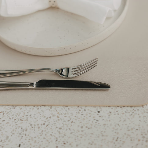 Cremefarbenes Platzset in Lederoptik mit Teller, Gabel und Messer auf gedecktem Tisch