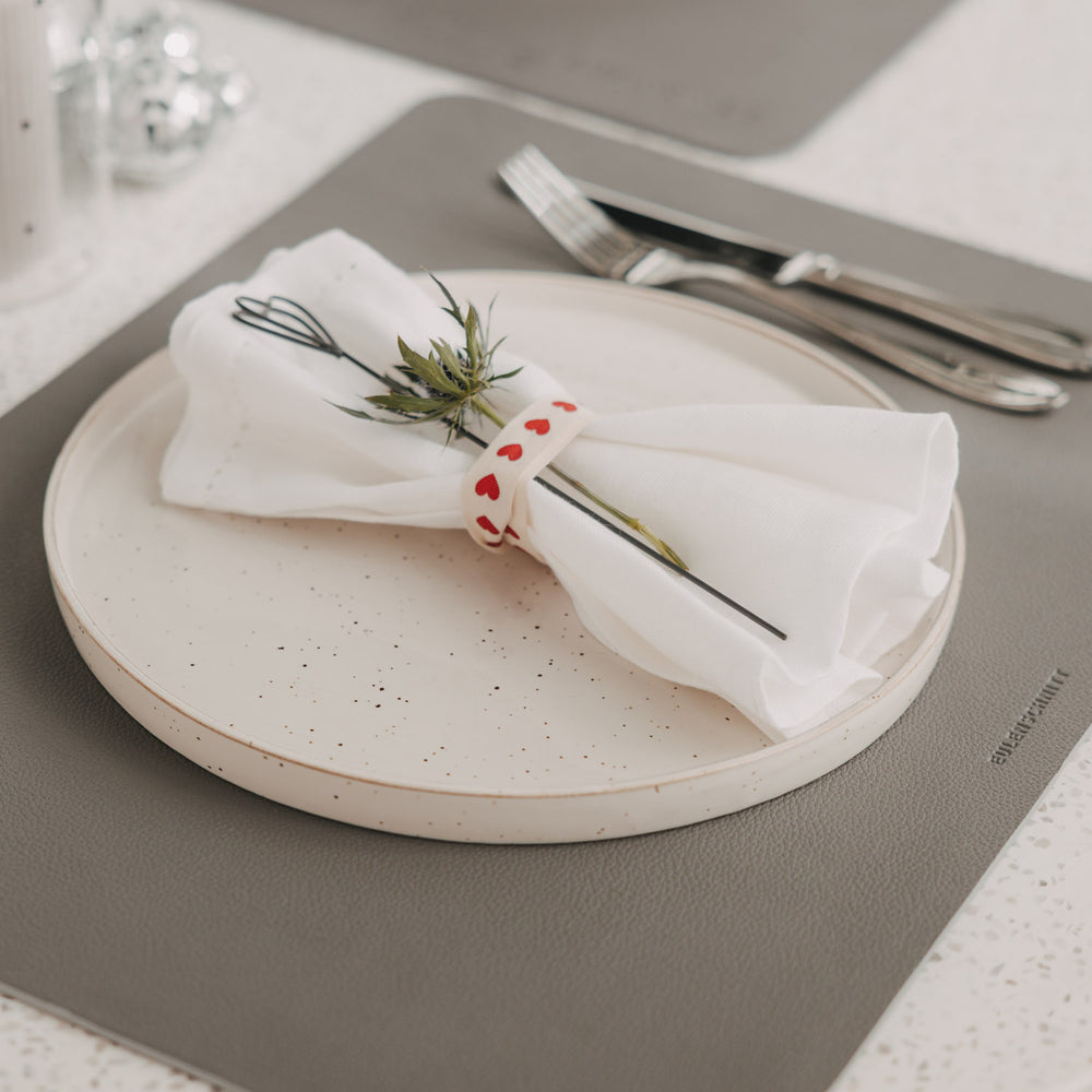 Dunkelgraues Platzset mit Teller, Serviette und Besteck auf gedecktem Tisch