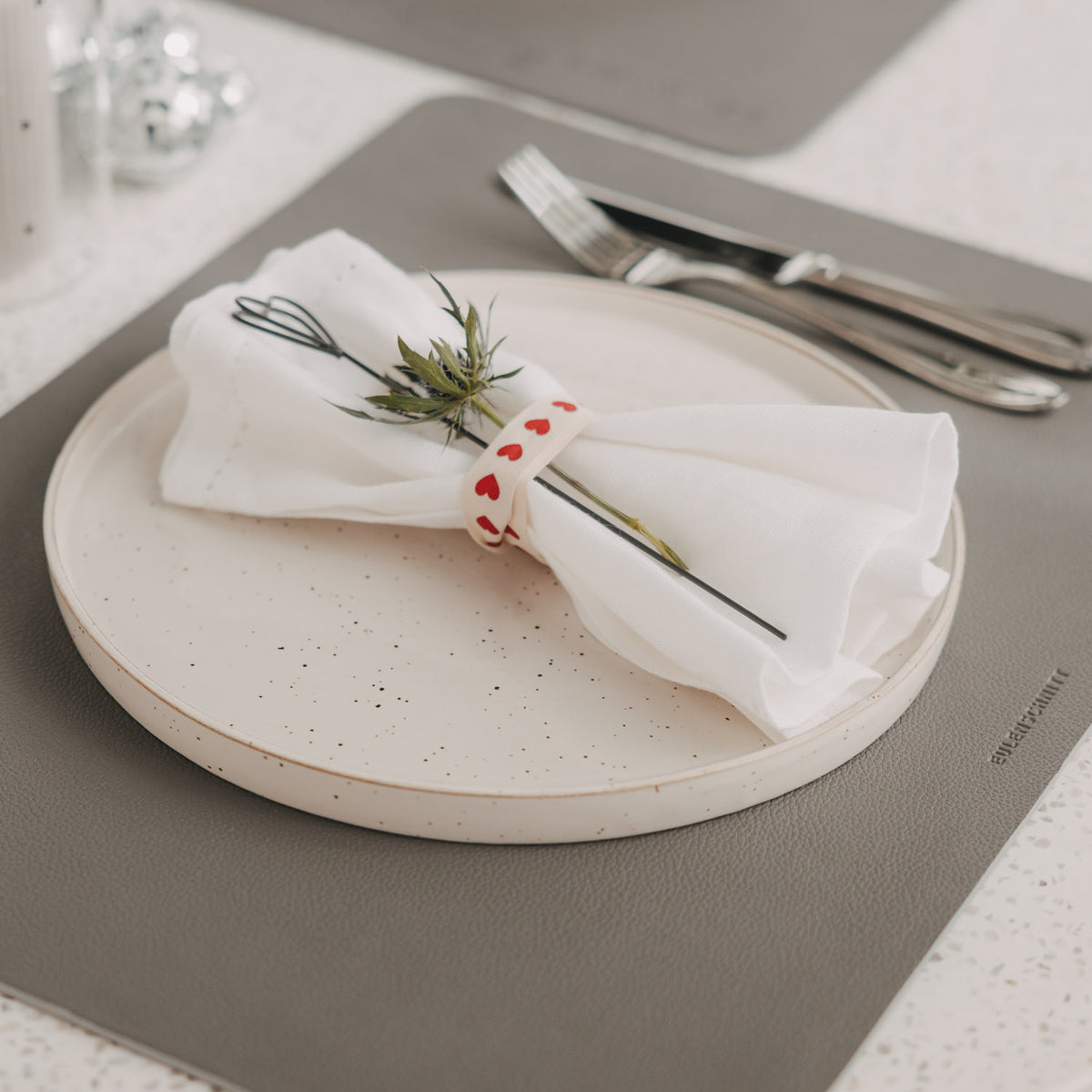 Dunkelgraues Platzset mit Teller, Serviette und Besteck auf gedecktem Tisch