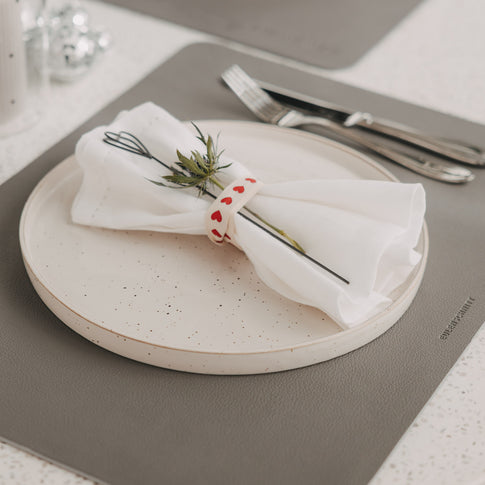 Dunkelgraues Platzset mit Teller, Serviette und Besteck auf gedecktem Tisch