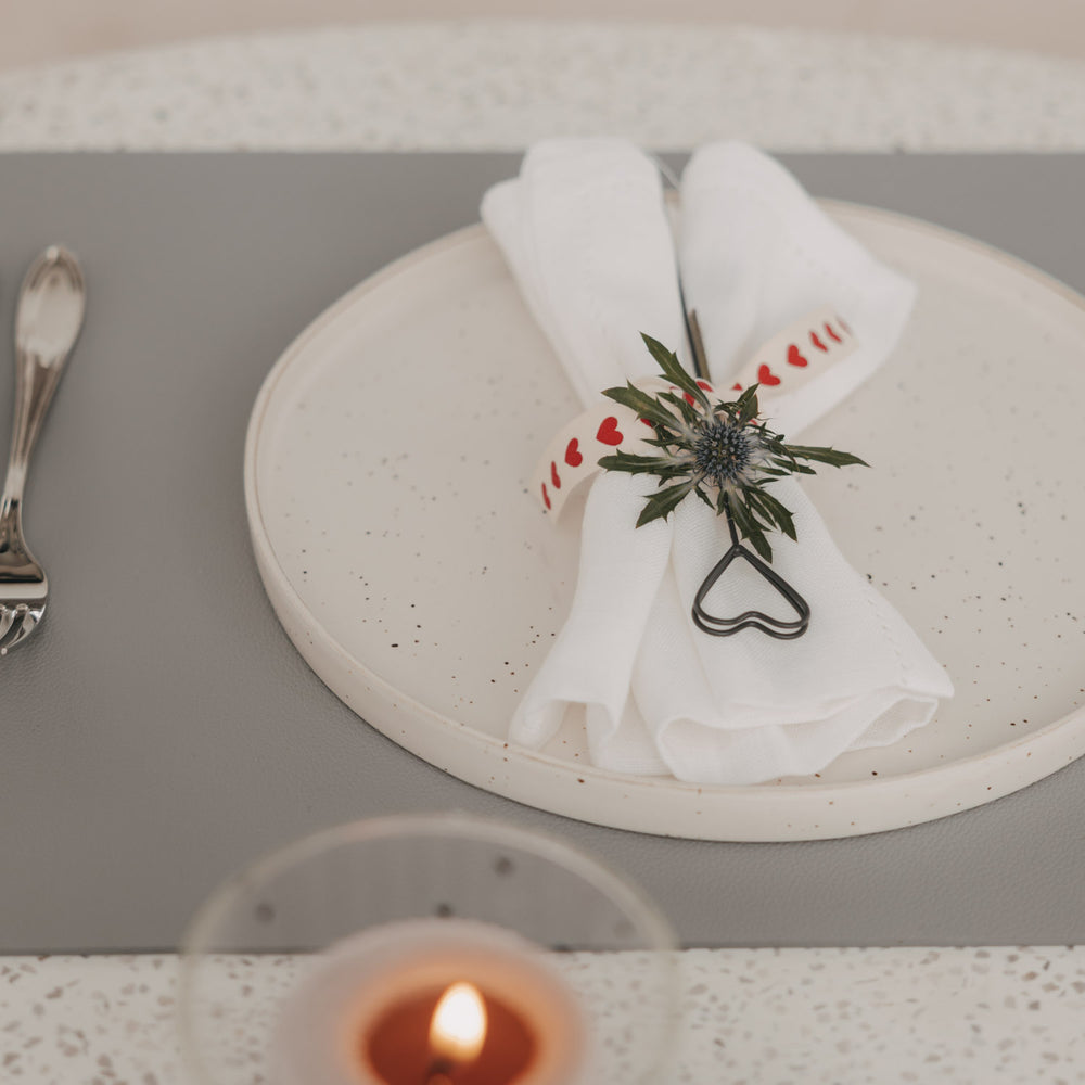 Graues Platzset mit Teller, weißer Serviette und herzförmigem Serviettenhalter