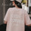 Rückansicht einer Frau im rosafarbenen „Iced Coffee Club“-T-Shirt mit heller Cap.