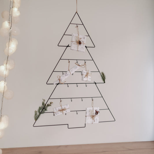 Adventskalender Tanne dekoriert mit kleinen Geschenken und Zweigen an der Wand.
