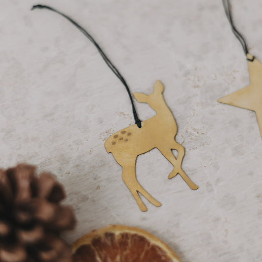 Detailaufnahme des goldenen Reh-Anhängers mit schwarzem Band, daneben Trockenscheiben und Zapfen.