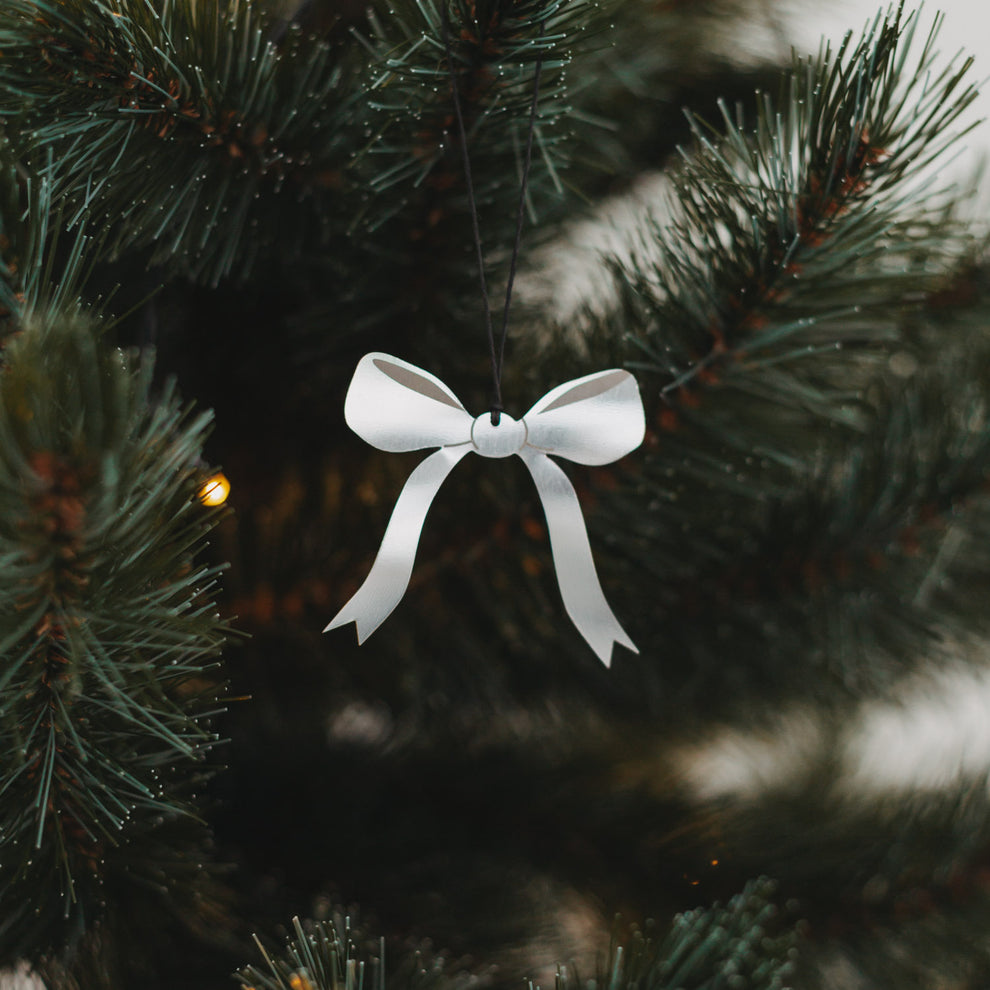 Silberner Schleifenanhänger aus Metall am Weihnachtsbaum mit Lichterkette, stilvoll und festlich dekoriert.