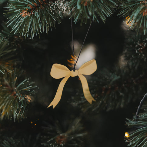 Goldener Schleifenanhänger aus Metall, aufgehängt an einem Tannenast mit warmem Lichterglanz.