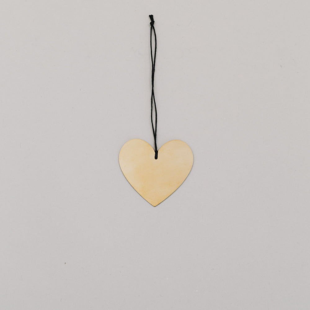 Herzförmiger goldener Metallanhänger mit schwarzem Band auf hellem Untergrund, flach ausgelegt.