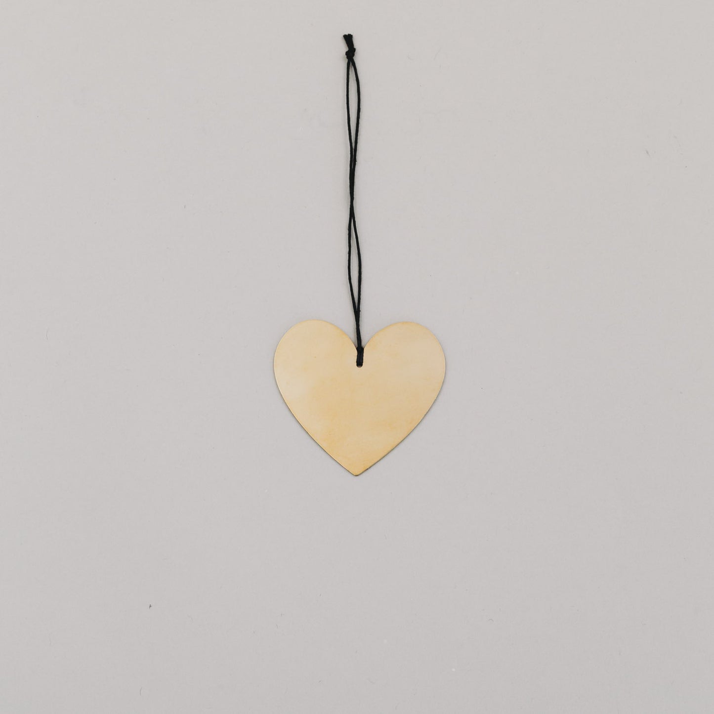 Herzförmiger goldener Metallanhänger mit schwarzem Band auf hellem Untergrund, flach ausgelegt.