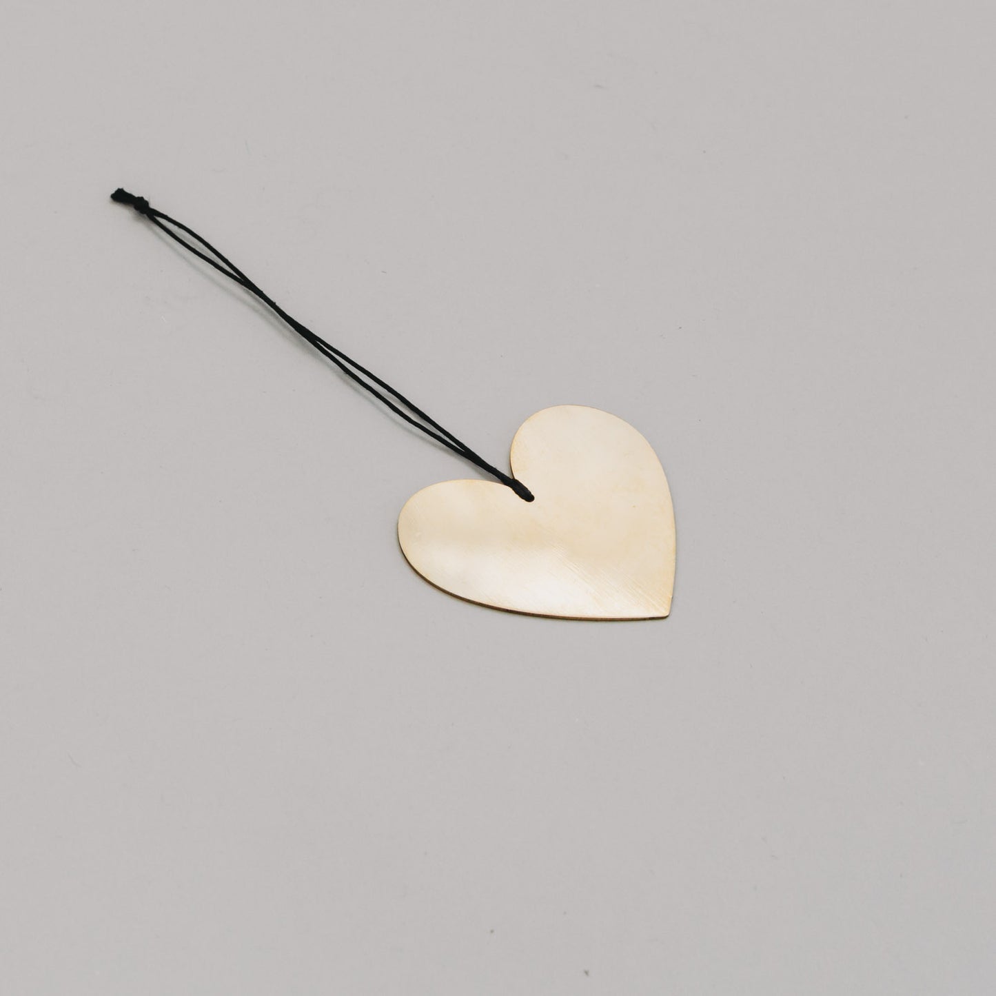 Goldenes Herz aus Metall mit schwarzem Band, leicht schräg liegend auf hellem Untergrund präsentiert.