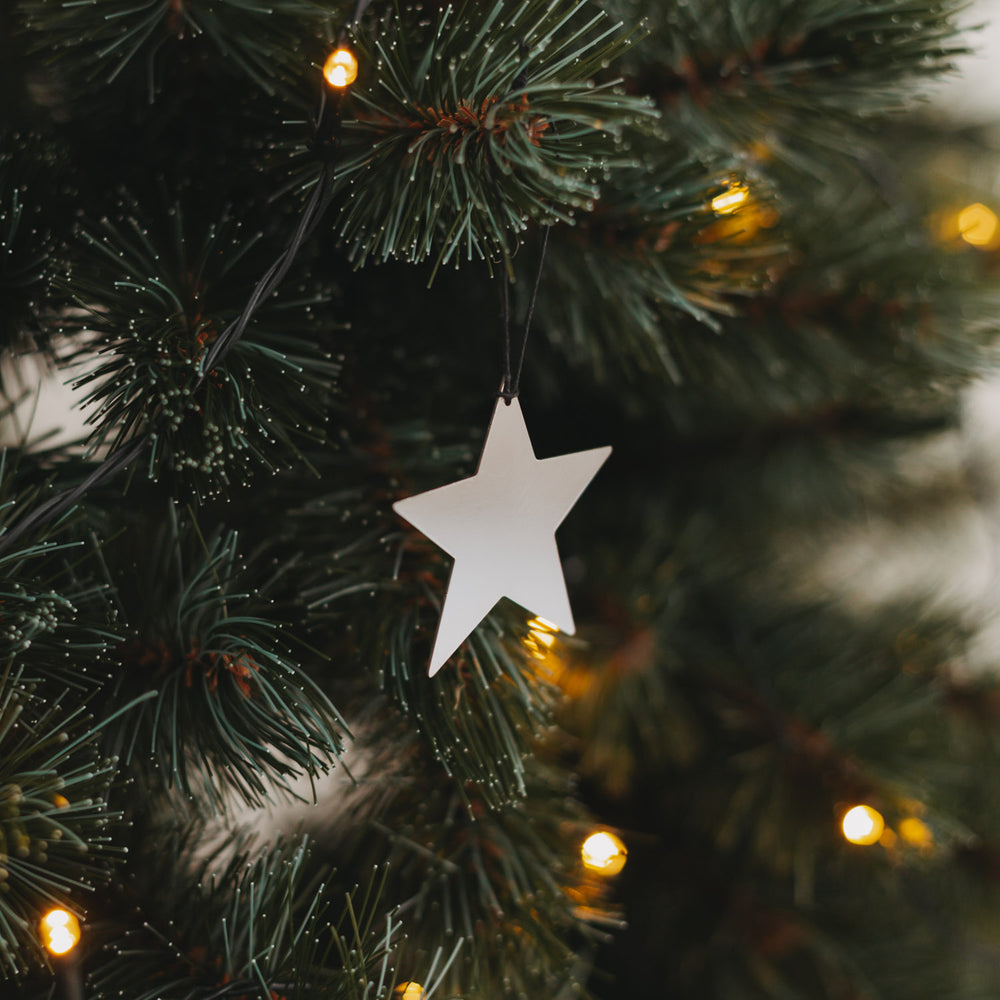Glänzender silberner Sternanhänger am Weihnachtsbaum mit feinen Lichterketten im Hintergrund.