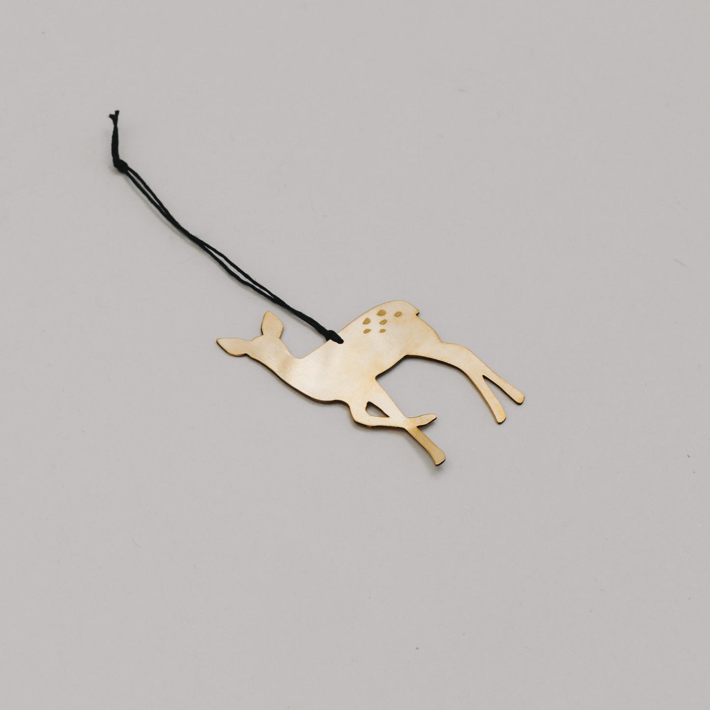 Schlichter goldener Rehanhänger aus Metall mit schwarzem Band, auf hellem Untergrund liegend.