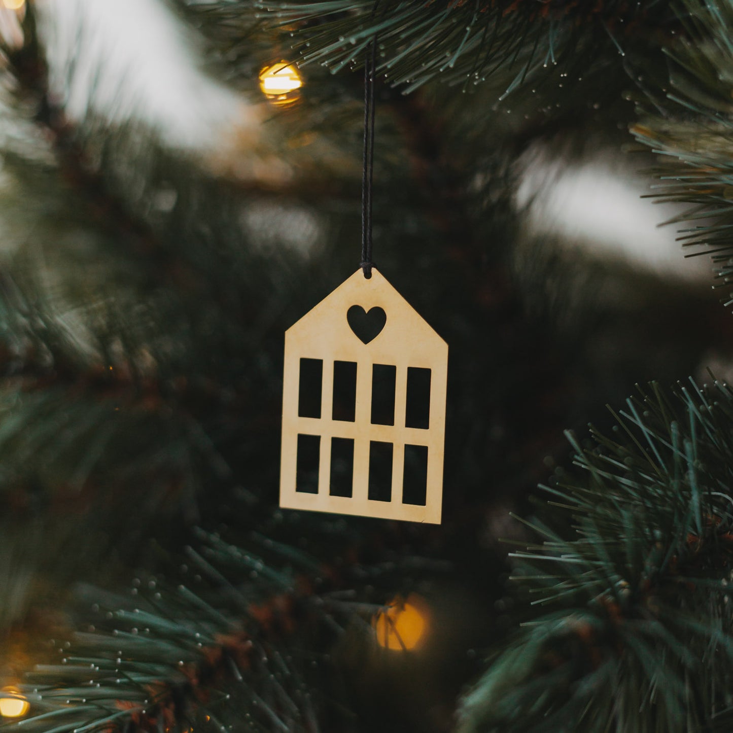 Goldener Hausanhänger  mit schwarzem Band an grünem Tannenzweig.