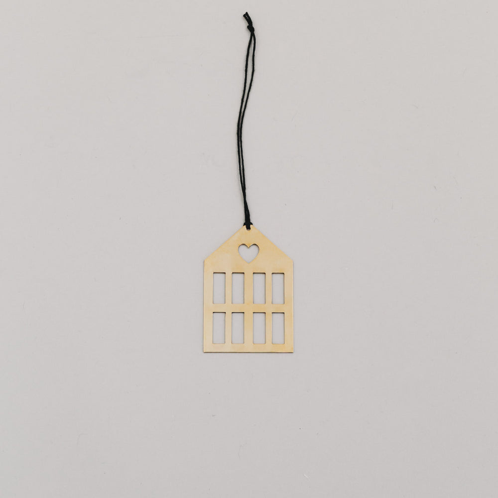 Goldener Hausanhänger aus Metall mit schwarzer Kordel auf hellem Hintergrund, minimalistisch arrangiert.