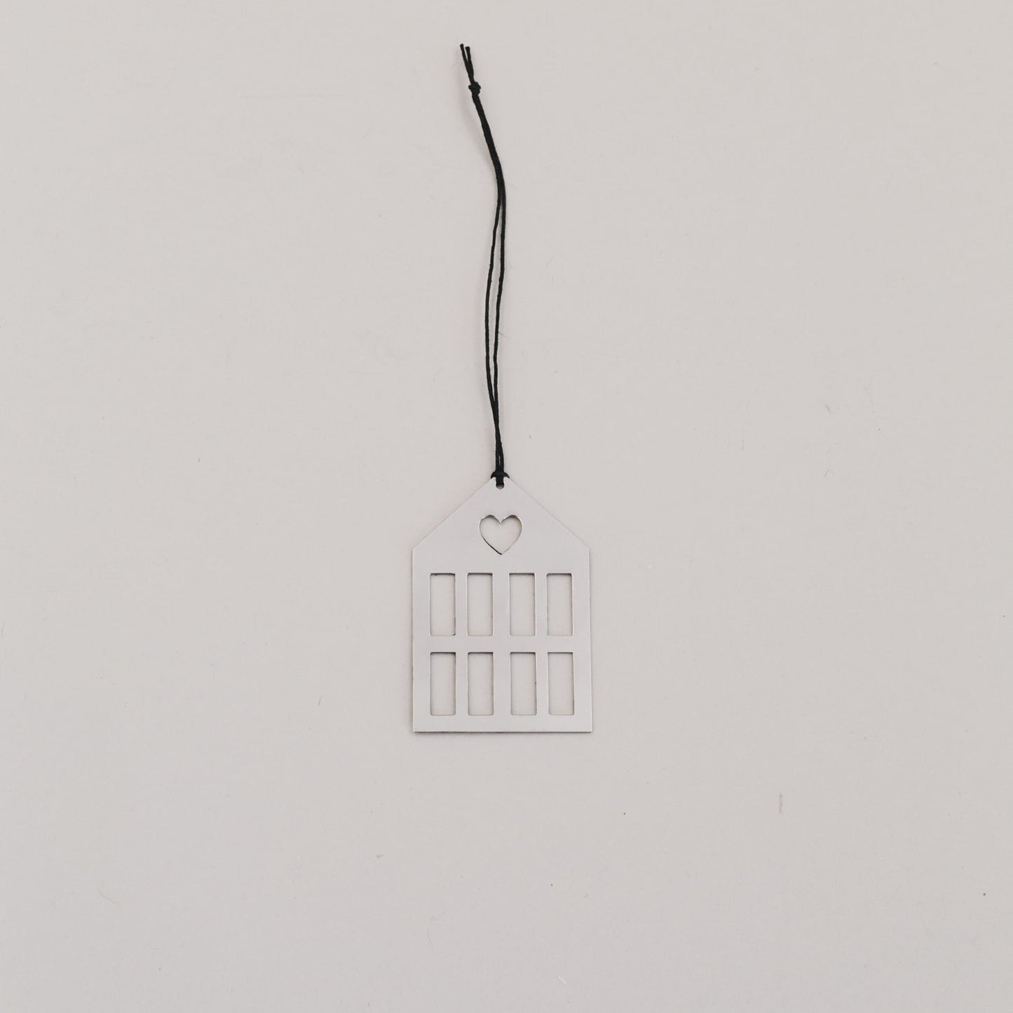 Silberner Hausanhänger aus Metall mit schwarzer Kordel auf hellem Hintergrund, minimalistisch arrangiert.