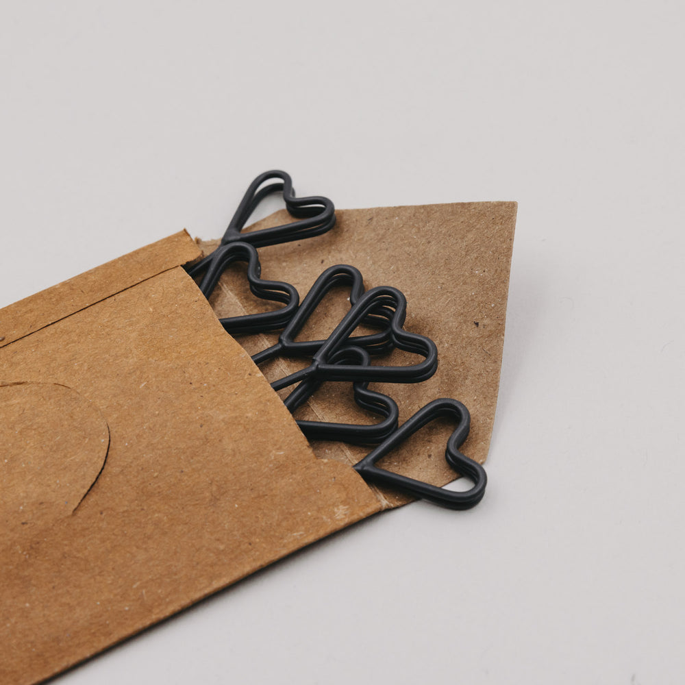 Mehrere schwarze Herz-Stecker ragen aus einer geöffneten braunen Papierverpackung.