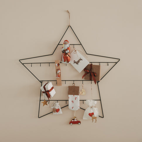 Adventskalender Stern groß aus Metall, dekoriert mit Geschenken, Karten und Anhängern an der Wand
